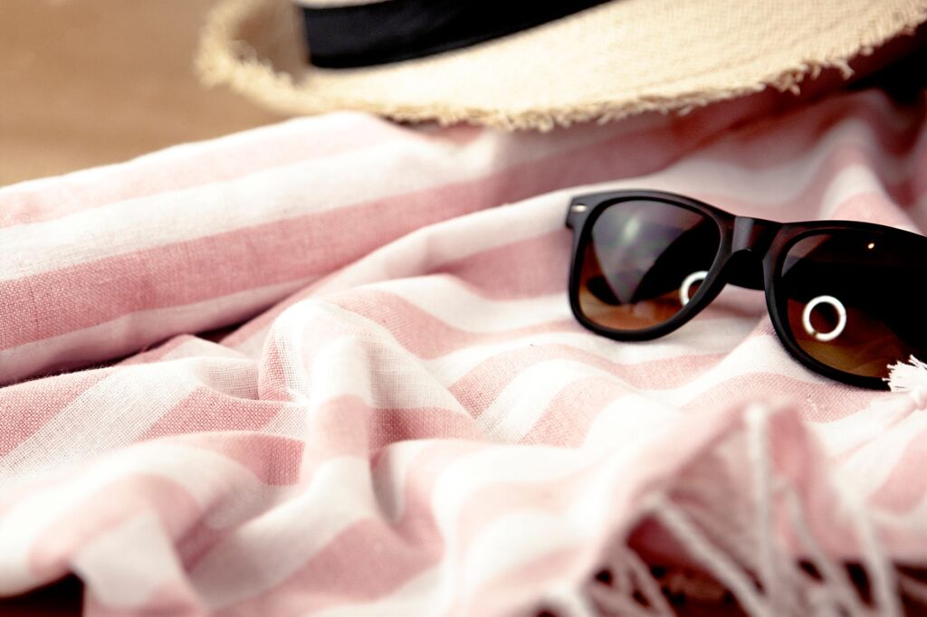 A stylish sun hat and sunglasses placed next to a beach towel. — packing list for Las Vegas summer